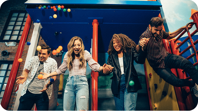 Four friends are playing on a colorful playground structure, laughing and enjoying playful interactions with bouncing balls.