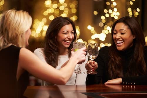 happy women friends toasting wine at a bar